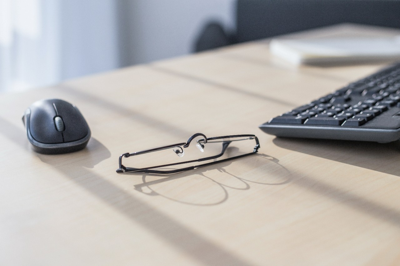 Closeup of laptop, glasses, coffee cup and other items on white desktop with blurry city in the background